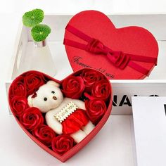 a teddy bear in a heart shaped box with roses and a bow on the top