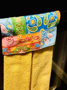 two yellow towels hanging on a rack in the oven with colorful paisley designs and colors