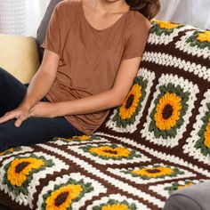 a woman sitting on top of a couch next to a blanket covered in sunflowers