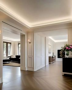 A modern hallway with white walls, crown molding, and wall panels. The floor is herringbone hardwood and there is recessed lighting in the ceiling. Modern Ceiling Trim, Wall Molding Hallway, Crown Molding With Lights, Paneling Hallway, Modern Moldings And Trim, White Crown Molding, Modern Crown Molding, Modern Crown, Herringbone Flooring