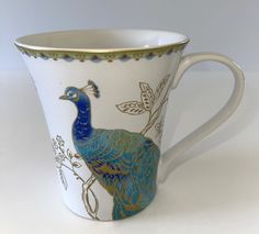 a coffee cup with a peacock painted on the side and gold trimming around the edge