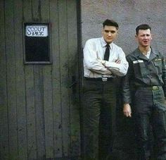 two men standing next to each other in front of a building with a sign on it