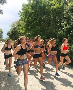 a group of young women running down a dirt road next to some bushes and trees