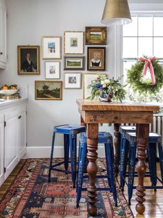 a dining room table with blue stools and pictures on the wall in front of it