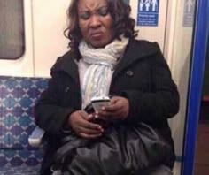 a woman sitting on a subway train looking at her cell phone while holding a purse