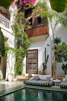 an outdoor pool surrounded by greenery and plants in front of a white building with wooden balconies