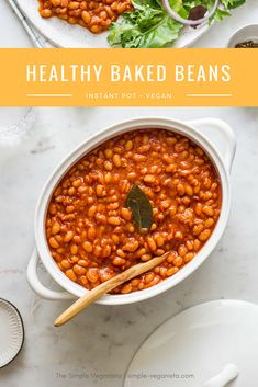 healthy baked beans in a white bowl with wooden spoons and salad on the side