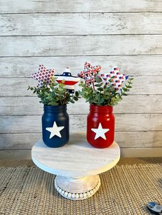 two red, white and blue mason jars with flowers in them sitting on a table