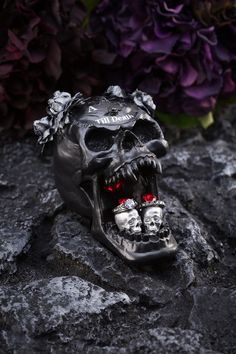 a black skull with red eyes and skulls on it's face sitting in front of purple flowers