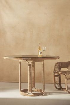 two wicker chairs and a table with a bottle of wine on it in front of a beige wall