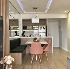 a dining room table with pink chairs next to a kitchen counter and an oven in the background