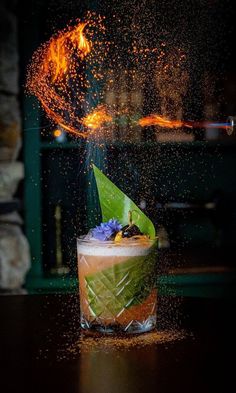 a drink is being sprinkled with orange and green liquid on a table in front of a fireplace