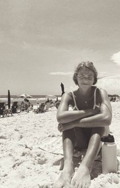 a woman is sitting on the beach with her legs crossed and arms folded over her chest