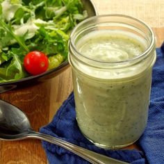 a salad in a bowl next to a jar of dressing on a table with a spoon