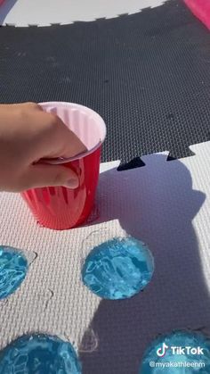 someone is holding a plastic cup with blue water in it and another person's hand on the table