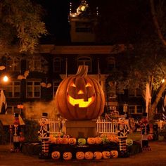 a large carved pumpkin sitting in the middle of a yard at night with decorations around it