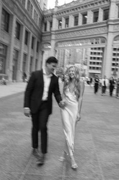 a man and woman walking in front of a large building with many people on it