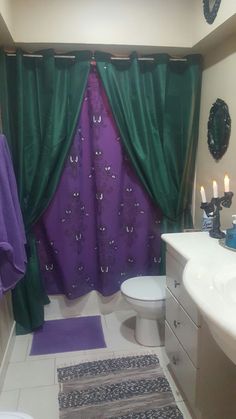 a purple and green shower curtain in a bathroom next to a white sink with candles on it