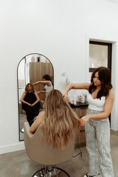 a woman is getting her hair done in a salon with another woman standing behind her