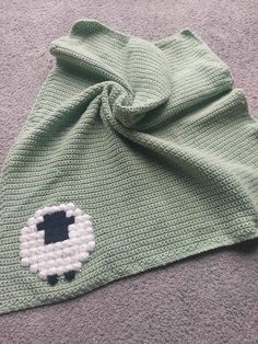 a green knitted hat with an embroidered sheep on the front and side, laying on carpet