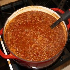 a red pot filled with chili sitting on top of a stove