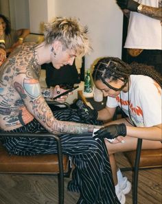 two people sitting in chairs with tattoos on their arms and legs, one is writing