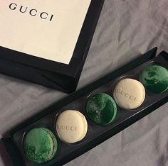 three green and white macaroons in a black box next to a gucci bag