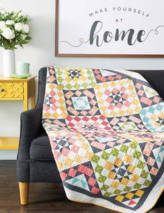 a couch with a quilt on it in front of a framed sign that says make yourself at home