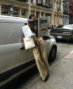 a man sitting on the back of a car while reading a newspaper in front of him