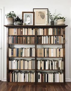 a bookshelf filled with lots of books next to a white wall and wooden floors