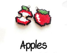 two apple shaped beaded charms sitting on top of a white sheet with the words apples written