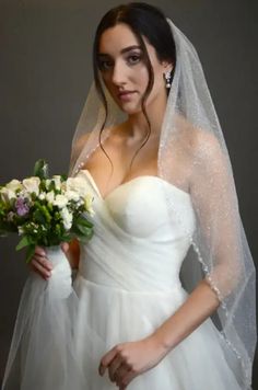 a woman in a white wedding dress holding a bridal bouquet and veil over her head