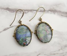 These dangle earrings are made with glass cabochons featuring the beautiful artwork of Claude Monet. A mixed pair, one earring shows Monet's famous waterlilies, the other shows a close-up of foliage in bloom. The cabochons are set against Art Nouveau floral brass filigree. The ear wires are solid brass. The earrings are 2" long from the top of the ear wires to the bottom of the dangles. Without the ear wires, the dangles are 1.25" long. These glass art cabochons were handmade by me. The cabochon Bohemian Oval Cabochon Earrings, Victorian Cabochon Drop Earrings, Vintage Cabochon Metal Earrings, Oval Cabochon Clip-on Earrings Gift, Monet Earrings, Monet's Garden, Cabochon Earrings, Brass Filigree, Art Nouveau Floral