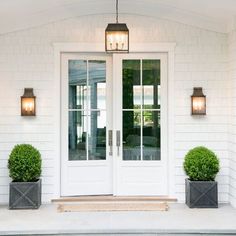 two potted plants sitting on the front steps of a white house with double doors