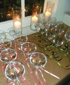 there are many wine glasses with pink ribbons on the table next to candles and flowers