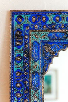 an intricately decorated mirror hanging on the wall next to a white wall with a blue frame