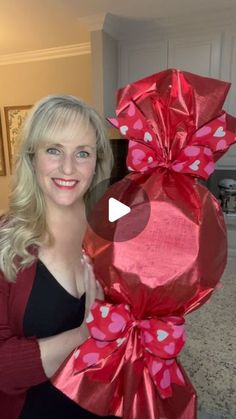 a woman is holding up a large red present wrapped in pink and red paper with hearts on it