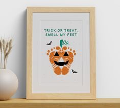 a wooden shelf with a framed poster on it and a vase next to it that says trick or treat, smell my feet