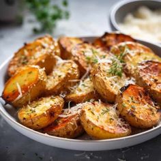 baked potatoes with parmesan cheese and herbs in a white bowl on a table