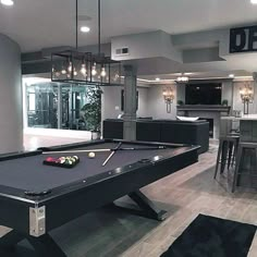 a pool table in the middle of a living room with stairs leading up to an open floor plan