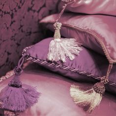 a purple pillow with tassels on it sitting next to a pile of pillows