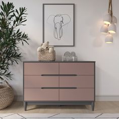 a pink dresser in a white room next to a plant and pictures on the wall