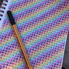 a pencil sitting on top of a notebook with an intricate pattern in the background and another pen laying next to it