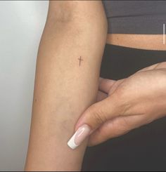 a woman's arm with a small cross tattoo on the left side of her arm