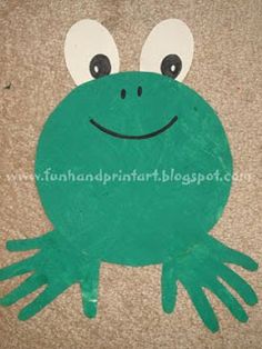 a green frog made out of foam on the ground with eyes and hands painted onto it