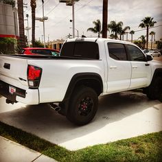 a white truck parked on the side of a road next to a palm tree filled parking lot