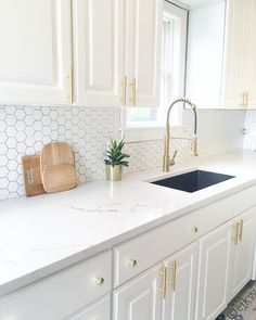 a white kitchen with marble counter tops and gold pulls on the faucet above the sink