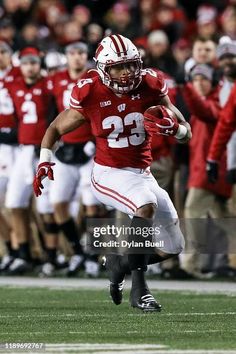 a football player running with the ball in his hand and other players behind him watching