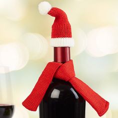 a bottle of wine with a santa hat on it and a glass of red wine next to it