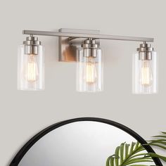 three light bathroom fixture with clear glass shades and metal frame, on a white wall